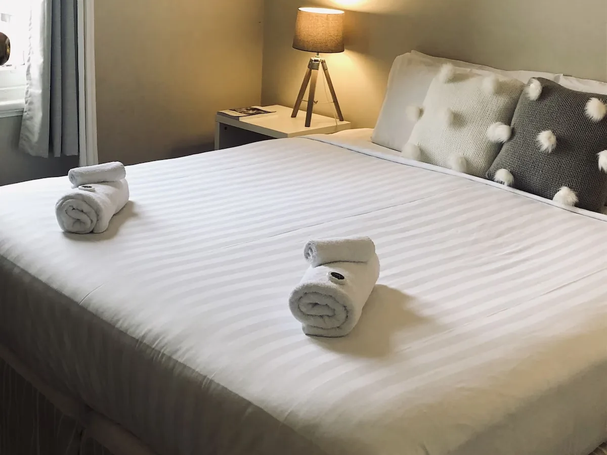 A guest room with a made-up bed, folded towels and a bedside lamp