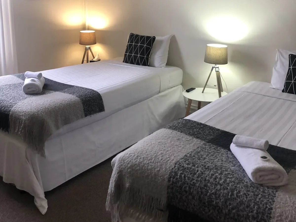 A guest room with two single beds, folded towels and bedside lamps
