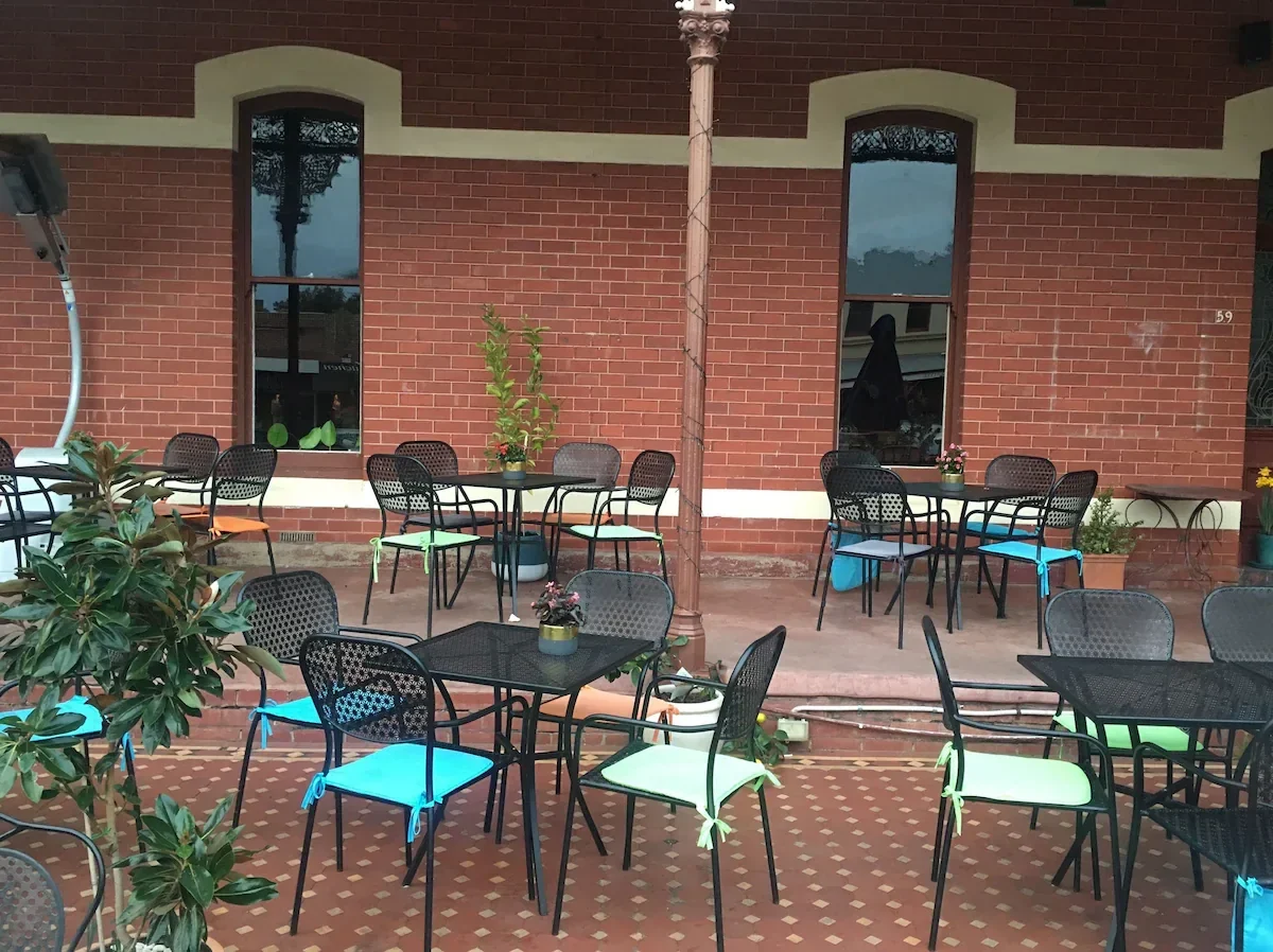 The front verandah, with black metal tables and chairs against the red-brick wall